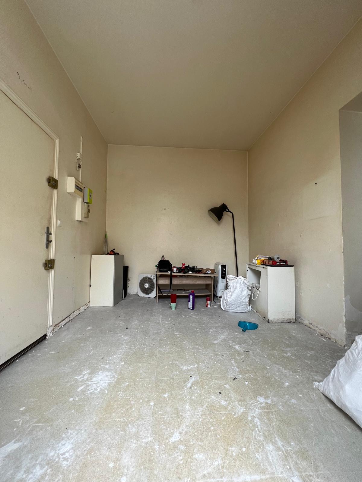 Pièce de vie d’un studio avant rénovation complète à Boulogne-Billancourt avec murs dégradés, sol brut à reprendre et finitions à rénover